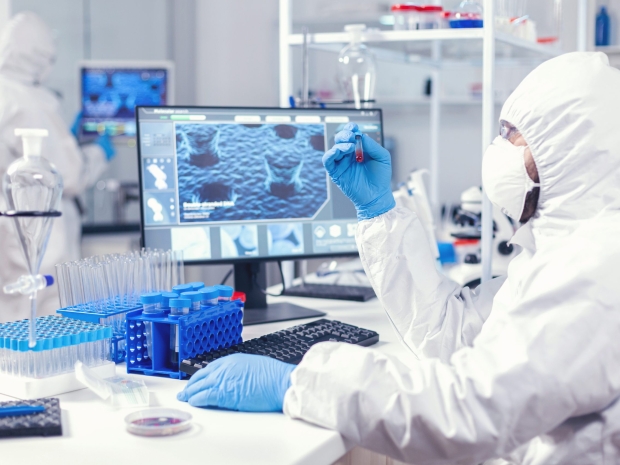 Scientist in protection suit holding sample of infected blood with coronavirus in test tube. Doctor working with various bacteria and tissue, pharmaceutical research for antibiotics against covid19.